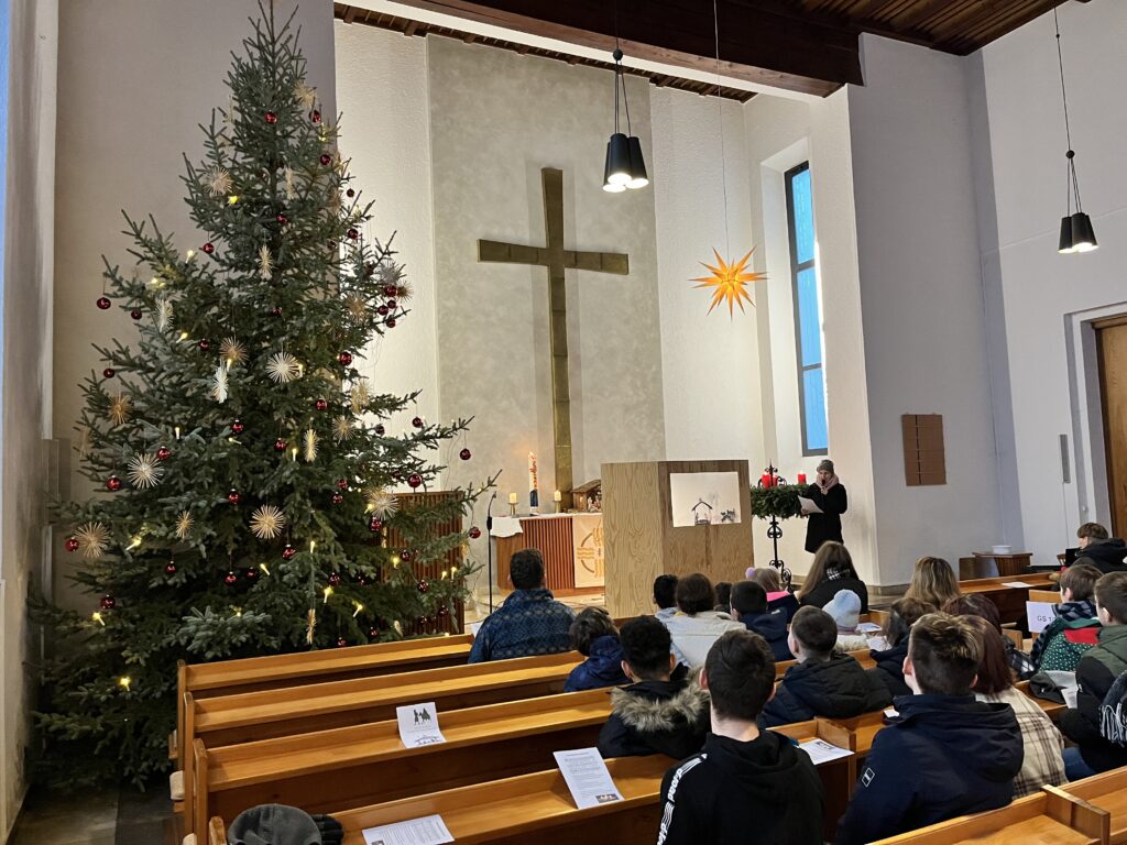 Kirchenraum mit Weihnachtsbaum, Kreuz, Schattenspiel und SchülerInnen in den Kirchenbänken