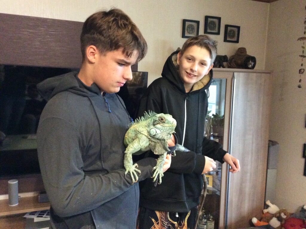 Zwei Schüler stehen da und eine hat einen Leguan auf dem Arm