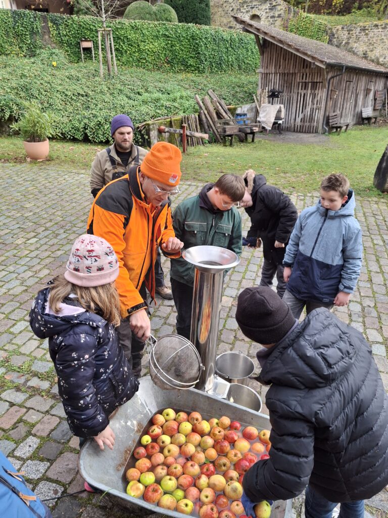 Schüler waschen äpfel und geben sie in eine Apfelquetsche
