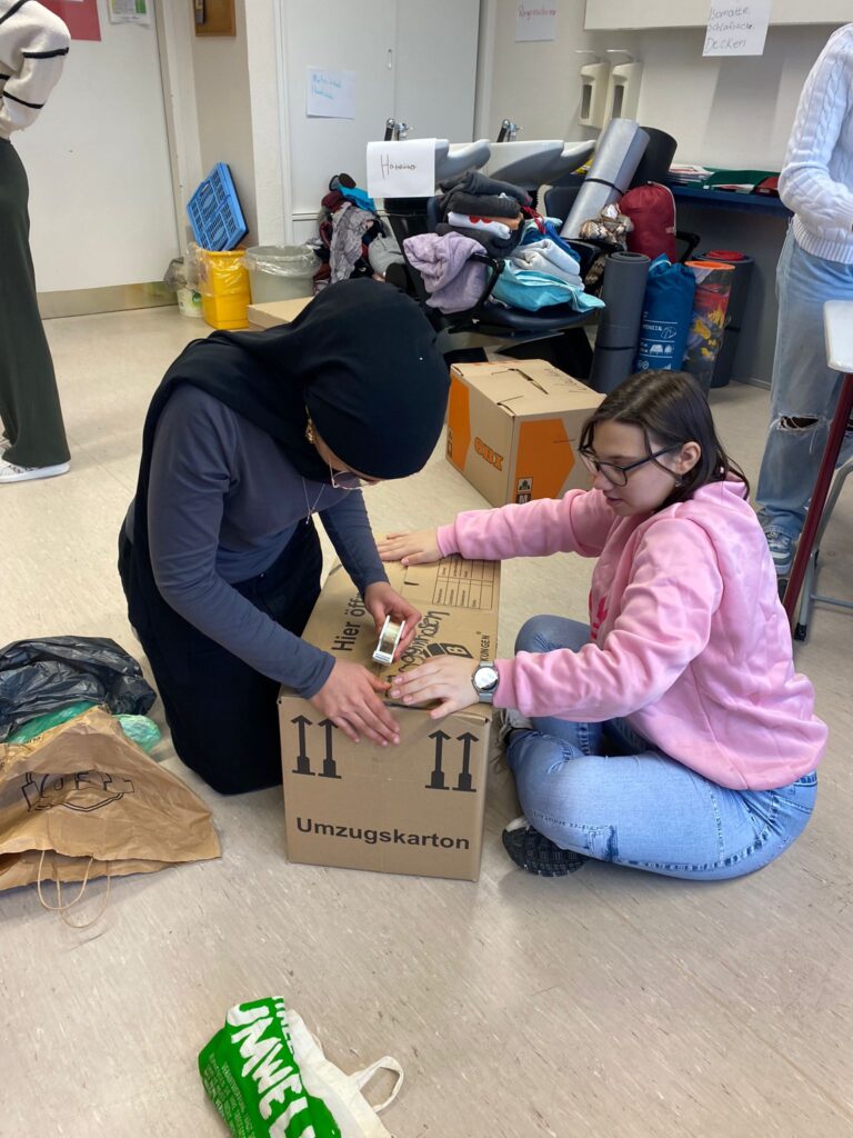 Zwei Schülerinnen verpacken Spenden in einem Karton