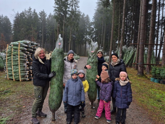Fünf SchülerInnen stehen mit ihren Lehrerinnen und Mitarbeitern der Baumschule Bob und zeigen ihre Weihnachtsbäume