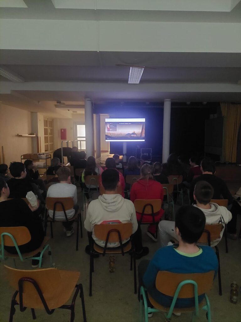 SchülerInnen sitzen im Mehrzweckraum auf Stühlen und schauen gemeinsam einen Film an