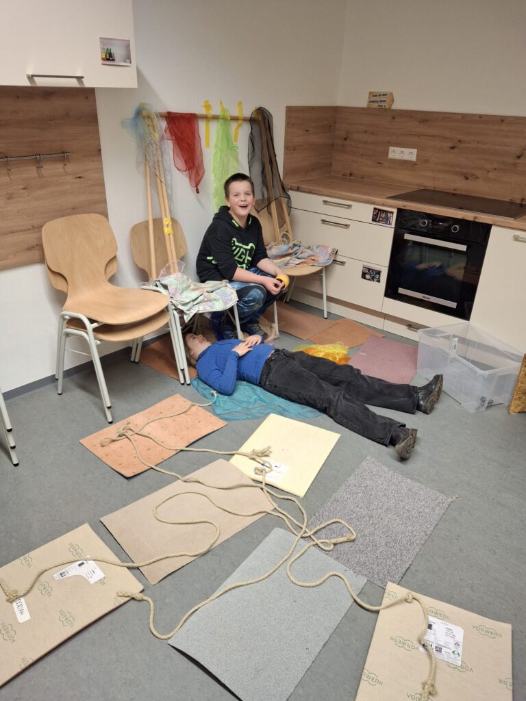 Ein Schüler und eine Schülerin zeigen Materialien des Projektes auf dem Boden der Schulküche