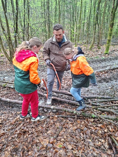 Zwei Schülerinnen sägen mit ihrem Lehrer Äste mit einer Handsäge klein