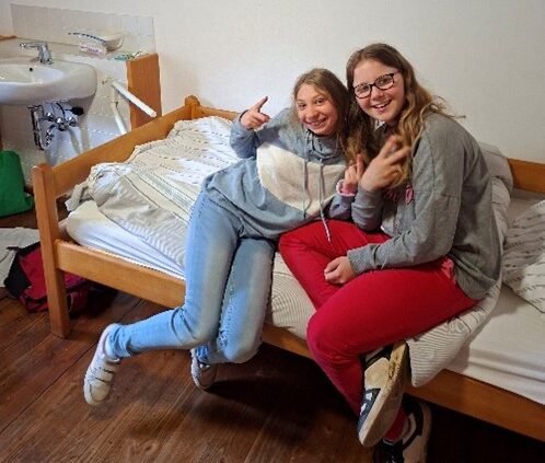 Zwei Schülerinnen sitzen freudig auf dem Bett der Landschulheims