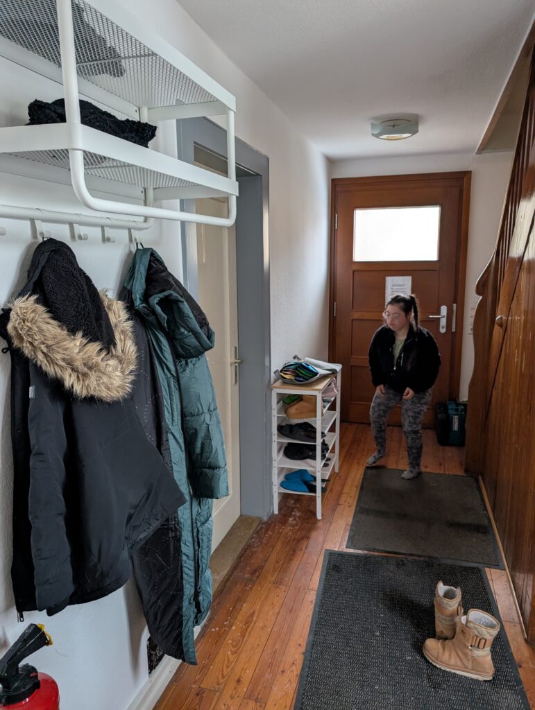 Eingangsflur des Trainingswohnhauses. Jacken hängen an der Garderobe und eine Schülerin steht im Gang